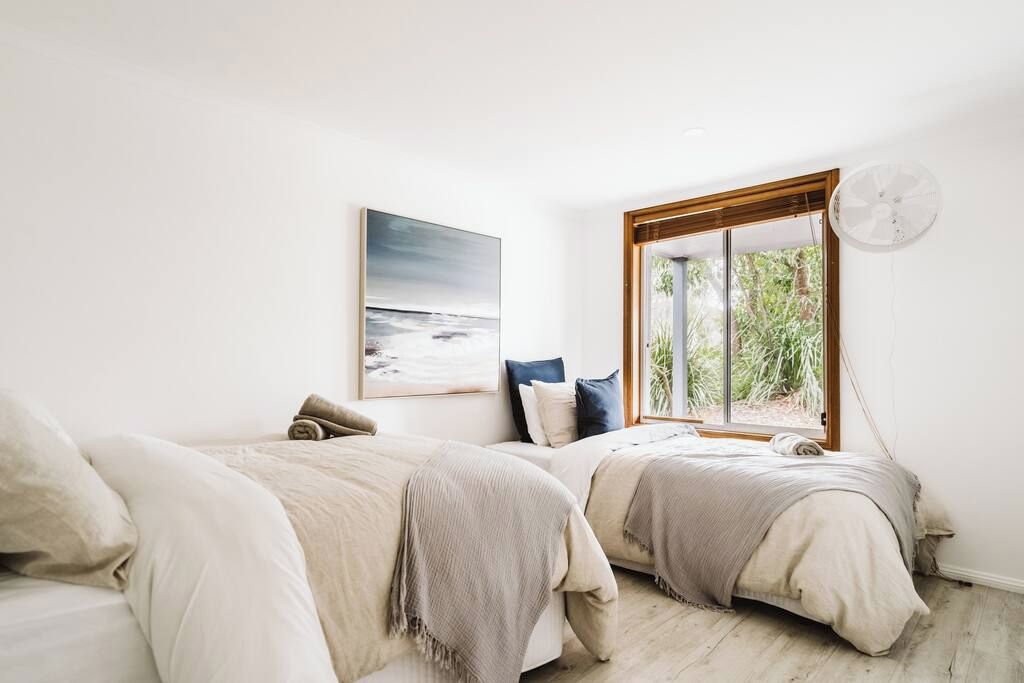Une chambre avec deux lits, une grande fenêtre donnant sur un paysage verdoyant et un ventilateur de plafond.