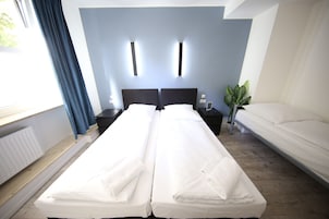 Una cama doble con sábanas blancas, una mesita de noche con lámpara y una planta en maceta.