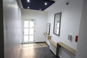 Un pasillo con una puerta, un espejo, un radiador y un estante con un cuadro enmarcado.