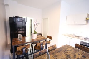 Cocina pequeña con una mesa y sillas de madera, un refrigerador negro y armarios blancos.