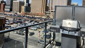 Blick vom Dach auf eine Stadtlandschaft mit modernen Gebäuden, einem Parkplatz und einem Grill.