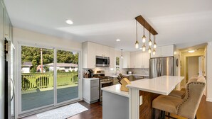 A modern kitchen with a large island, stainless steel appliances, and a sliding glass door to the backyard.