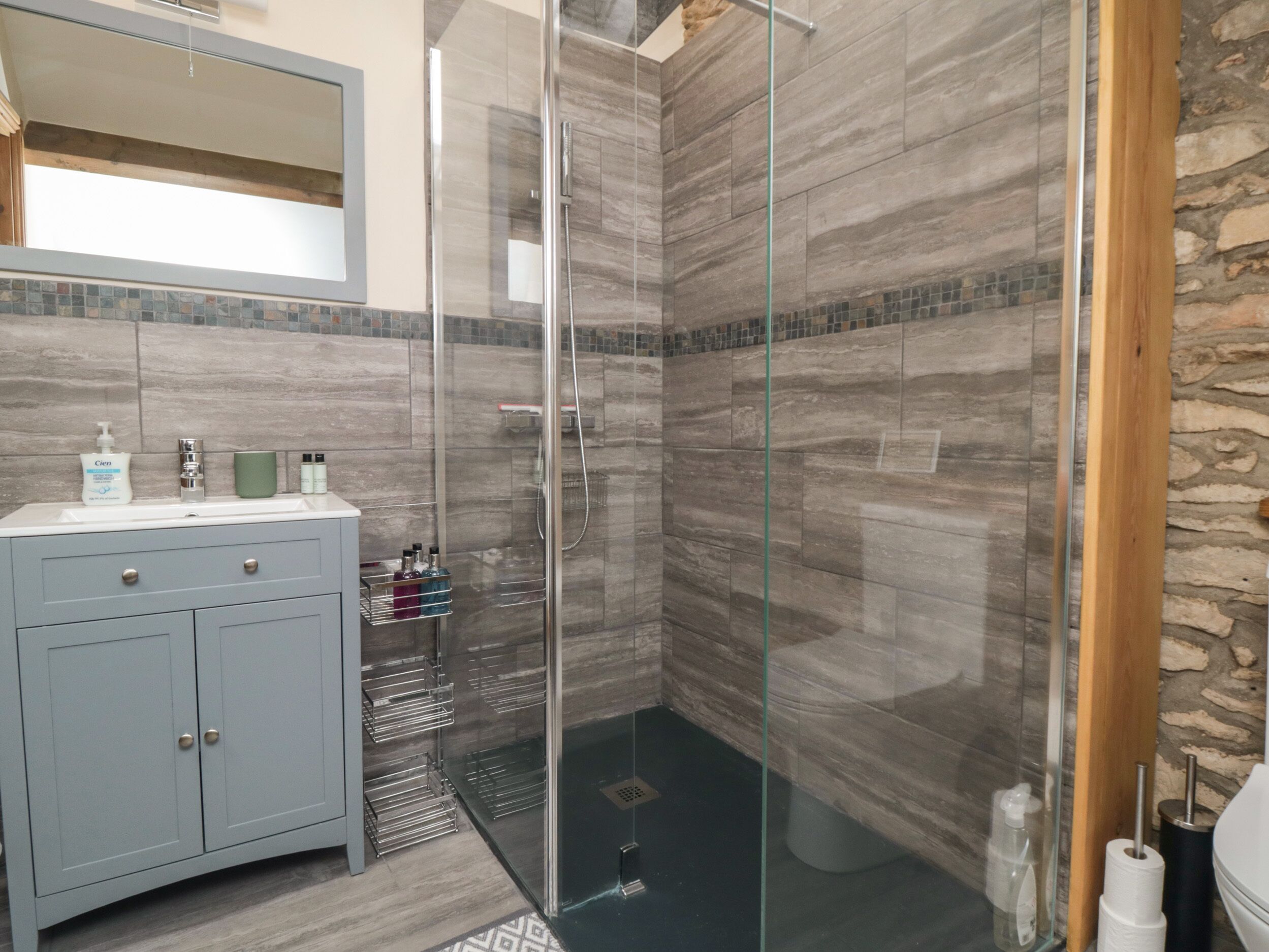 A modern bathroom with a glass shower enclosure, a vanity with a mirror, and toiletries on the counter.