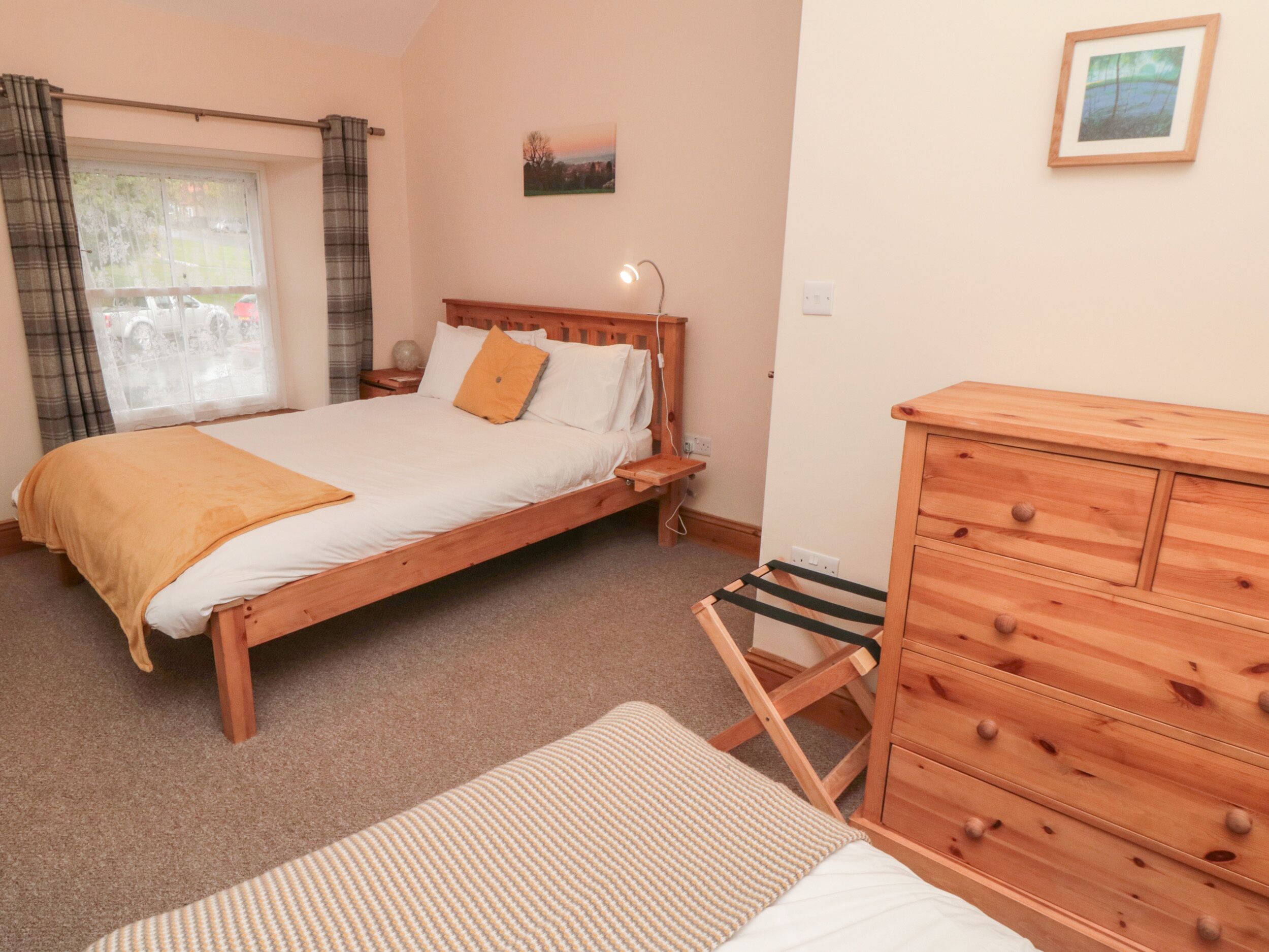 Un dormitorio con cama, cómoda de madera, mesita de noche, ventana con cortinas e imagen colgada en la pared.
