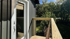 Una terraza de madera con barandilla metálica, una puerta con ventanal y un toldo negro.