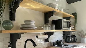 Una cocina moderna con estantes de madera, un grifo negro, un fregadero, un microondas y una cafetera.