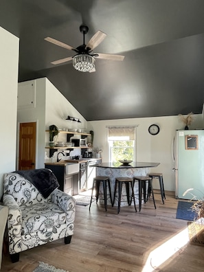 Une cuisine moderne avec un coin repas, dotée d’un ventilateur de plafond, d’un réfrigérateur et d’une fenêtre avec des rideaux.