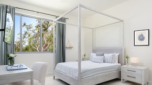 Une chambre moderne avec un lit à baldaquin, un bureau avec une chaise, une table de chevet avec une lampe et une fenêtre avec des rideaux.