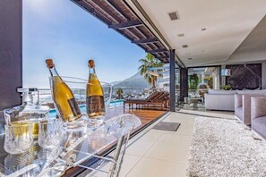 Uma sala de estar moderna com uma mesa de vidro exibindo garrafas e copos, uma piscina e vista para uma montanha.