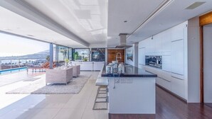 A modern kitchen with a central island, white cabinetry, and a view of the outdoors. - SaltLife Camps Bay, Modern luxury, incredible views & Prime location (Cape Town)