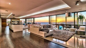 Un amplio espacio habitable con un gran ventanal que ofrece vistas al atardecer, una cocina moderna y una zona de estar acogedora con alfombra.