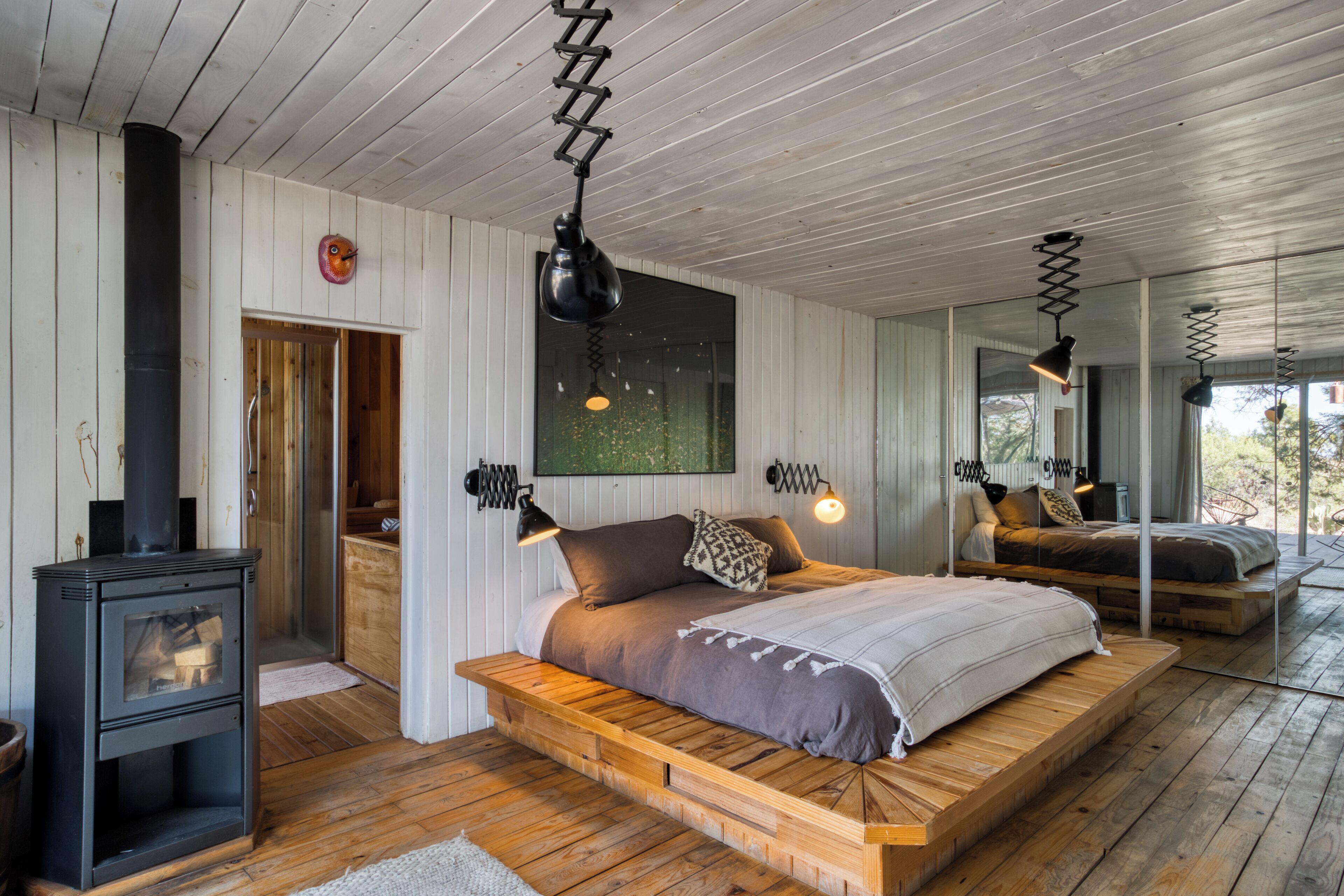 Ein Schlafzimmer mit einem hölzernen Plattformbett, einem schwarzen Kaminofen und moderner Pendelleuchten.