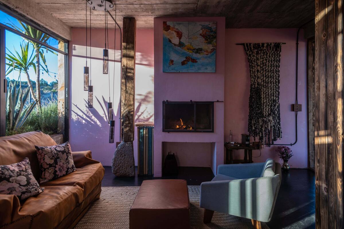 Uma sala de estar com lareira, um sofá, uma poltrona e uma janela grande com vista para o verde.