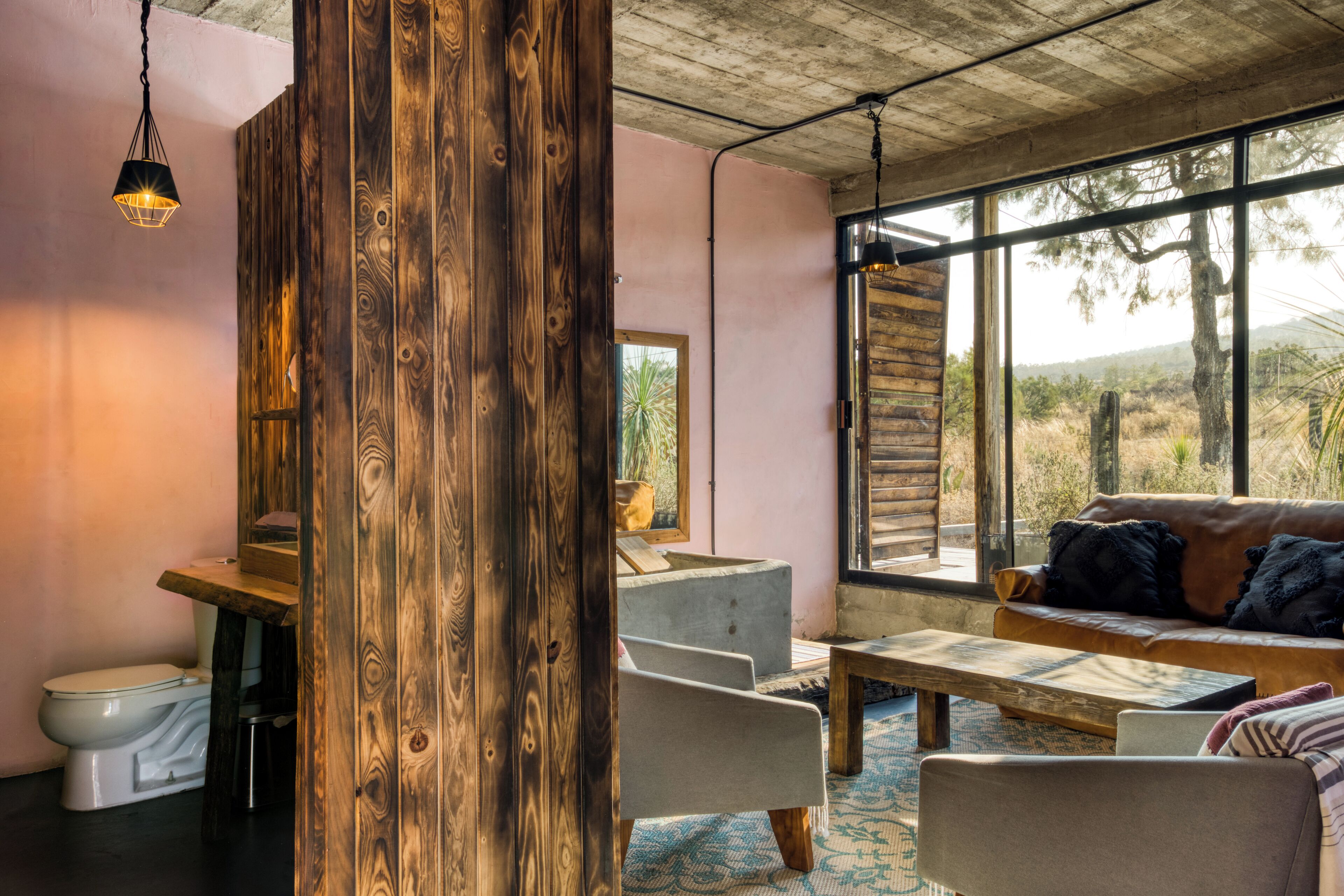 Un interno rustico con una parete in legno, un divano, un tavolo da pranzo e vista sull'esterno.