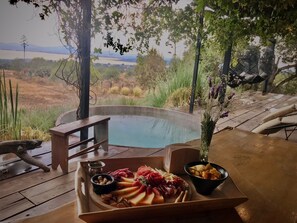 Una mesa de madera con una bandeja de comida, un jacuzzi y vistas a un paisaje natural.