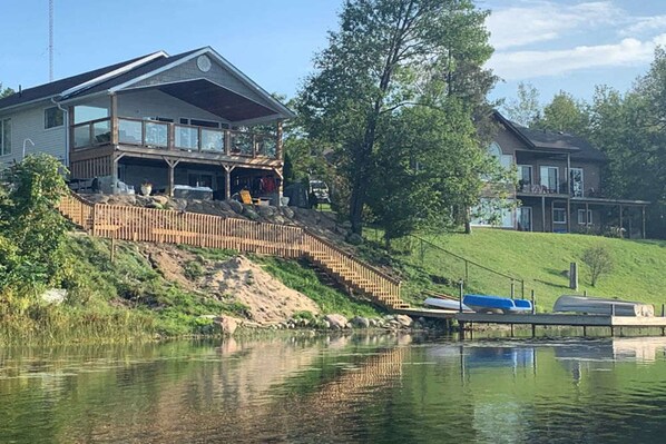 A two-story house with a deck and a dock extending into a calm lake.
