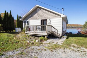 A single-story cabin with a porch, a small deck, and a view of a lake.