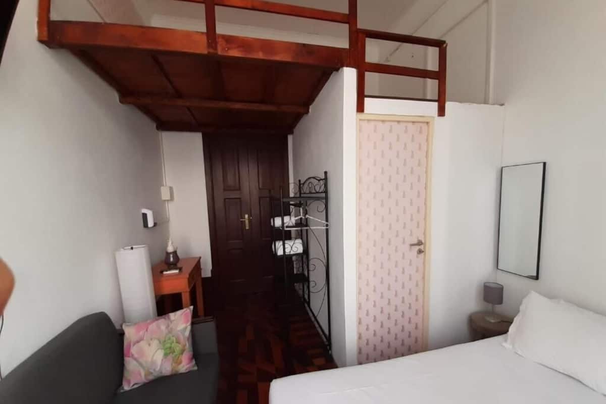 A room with a bed, a sofa, a wooden loft, a wardrobe, a mirror, and a patterned wall.