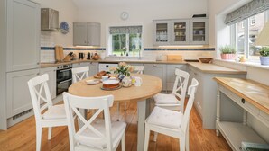 Une cuisine moderne avec des meubles blancs, une table à manger en bois et des chaises blanches, et une fenêtre donnant sur un paysage verdoyant.