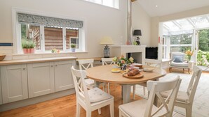 Une cuisine spacieuse avec des meubles blancs, une table à manger ronde en bois et des chaises blanches. Une fenêtre offre une vue sur la verdure à l’extérieur.