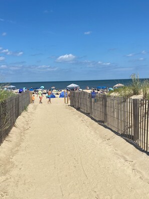 Un sentiero sabbioso che conduce all'oceano, con ombrelloni da spiaggia e persone.