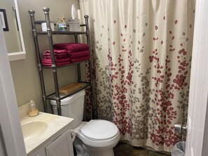 Un bagno con il water, un lavandino, uno scaffale con asciugamani e una tenda da doccia con motivo a foglie.