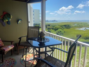 Un balcone con tavolo e sedie, un pesce decorativo e vista su un paesaggio verde e l'acqua.