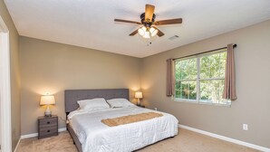 Un dormitorio con cama, mesitas de noche, ventilador de techo y ventana con cortinas.