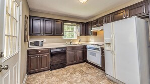 Una cocina con armarios de madera oscura, un refrigerador blanco, un microondas, un lavavajillas y una estufa.