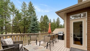 Une terrasse dotée de mobilier d’extérieur, d’un barbecue et offrant une vue sur les arbres.