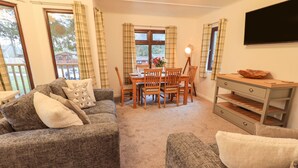 A cozy living room with a sofa set, a dining table with chairs, and a TV mounted on the wall. - Woodland Retreat (Windermere)