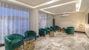 Una habitación de hotel moderna con piso de mármol, sillones de terciopelo verde y una mesa de centro redonda.