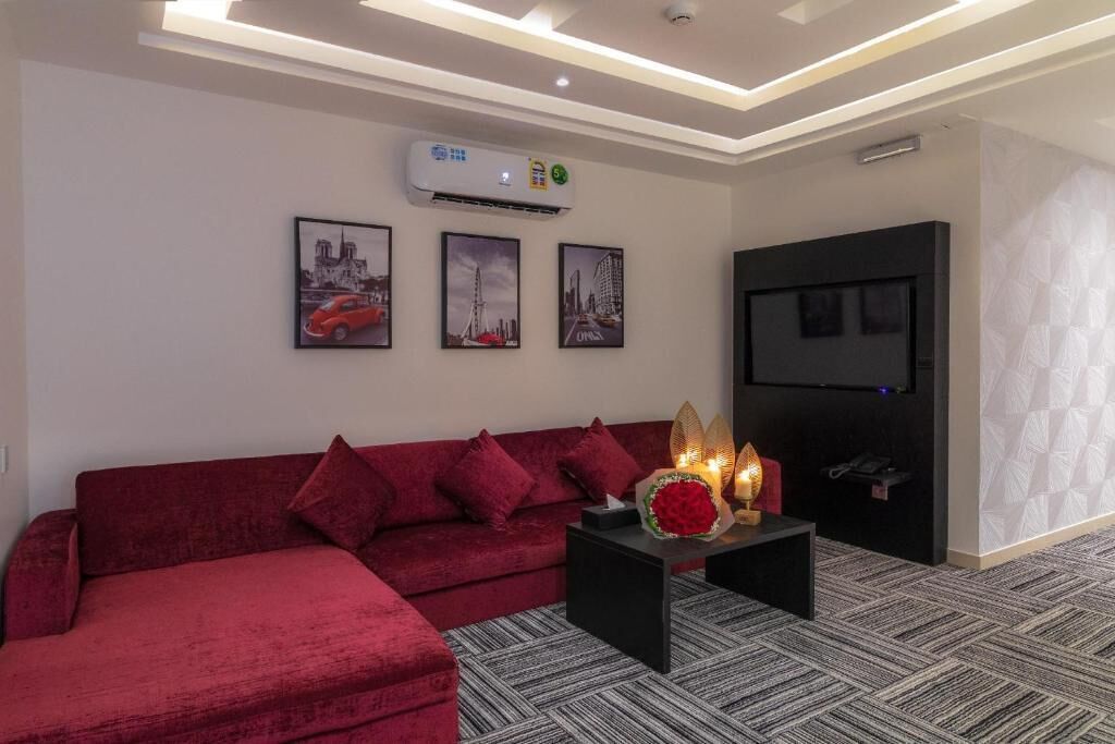 Un salón moderno con un sofá rojo, una mesa de centro negra con un jarrón de flores y un televisor de pantalla plana montado en una pared negra.