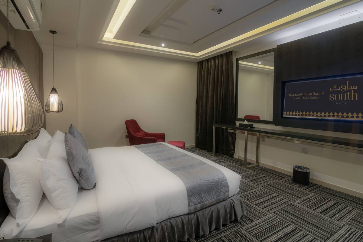 A hotel room with a bed, a red chair, a desk, and a large mirror.