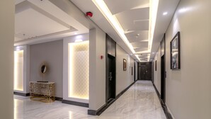 Un pasillo moderno de hotel con piso de mármol, iluminación empotrada y obras de arte enmarcadas en las paredes.