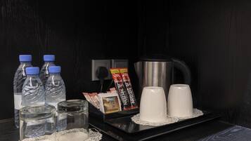 Una bandeja con botellas de agua, una cafetera y dos tazas blancas sobre una mesa negra.