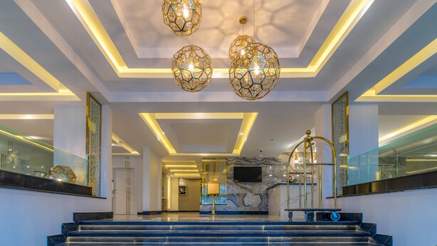 Un moderno vestíbulo de hotel con una escalera de mármol, diseño geométrico en el techo y lámparas esféricas colgantes.