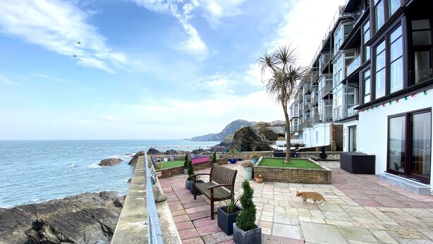 A coastal terrace with a stone pathway, seating area, and a view of the sea.