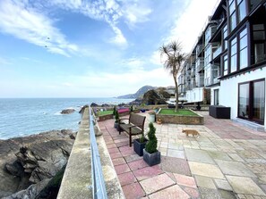A coastal terrace with a stone pathway, seating area, and a view of the sea. - 1 Cheyne Beach Apartments (Ilfracombe)