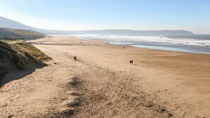 A wide sandy beach with gentle waves, a clear sky, and distant mountains.