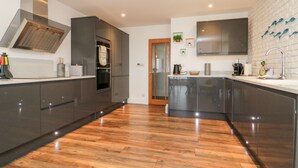 A modern kitchen with dark cabinetry, a stainless steel range hood, and a large island with a sink.