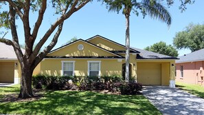 A yellow two-story house with a garage, surrounded by a well-maintained lawn and trees. - MEGA VALUE! Serenity By The Pool! Close 2 Disney! 1445 (Clermont)
