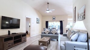 Una sala de estar con televisor de pantalla plana, ventilador de techo y sofá con almohadones decorativos.