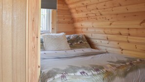 A cozy room with wooden walls, a bed with a floral bedspread, and a window with blinds. - Joshua's Den - UK40975 (Near Swansea)