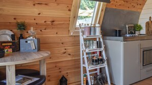 A cozy kitchen with wooden walls, a small dining table, and a white ladder shelf with kitchen items. - Joshua's Den - UK40975 (Near Swansea)