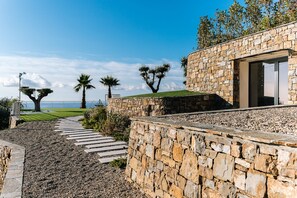 Un sendero de piedra que conduce a un edificio moderno con un muro de piedra y vista al mar.