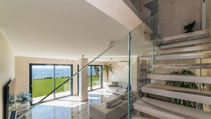 Un intérieur moderne avec un escalier en verre, un espace de vie doté d’un canapé et une vue sur l’océan.