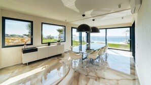 Une cuisine moderne avec une table à manger en verre, de grandes fenêtres et une vue sur la mer.