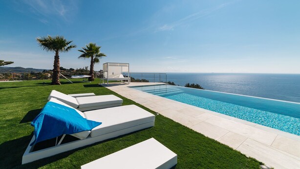 Un espace aménagé au bord de la piscine, avec vue sur l’océan, un coin salon couvert et une pelouse bien entretenue.