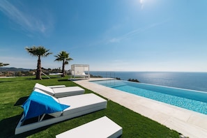 A poolside area with a view of the ocean, a covered seating area, and a well-maintained lawn.